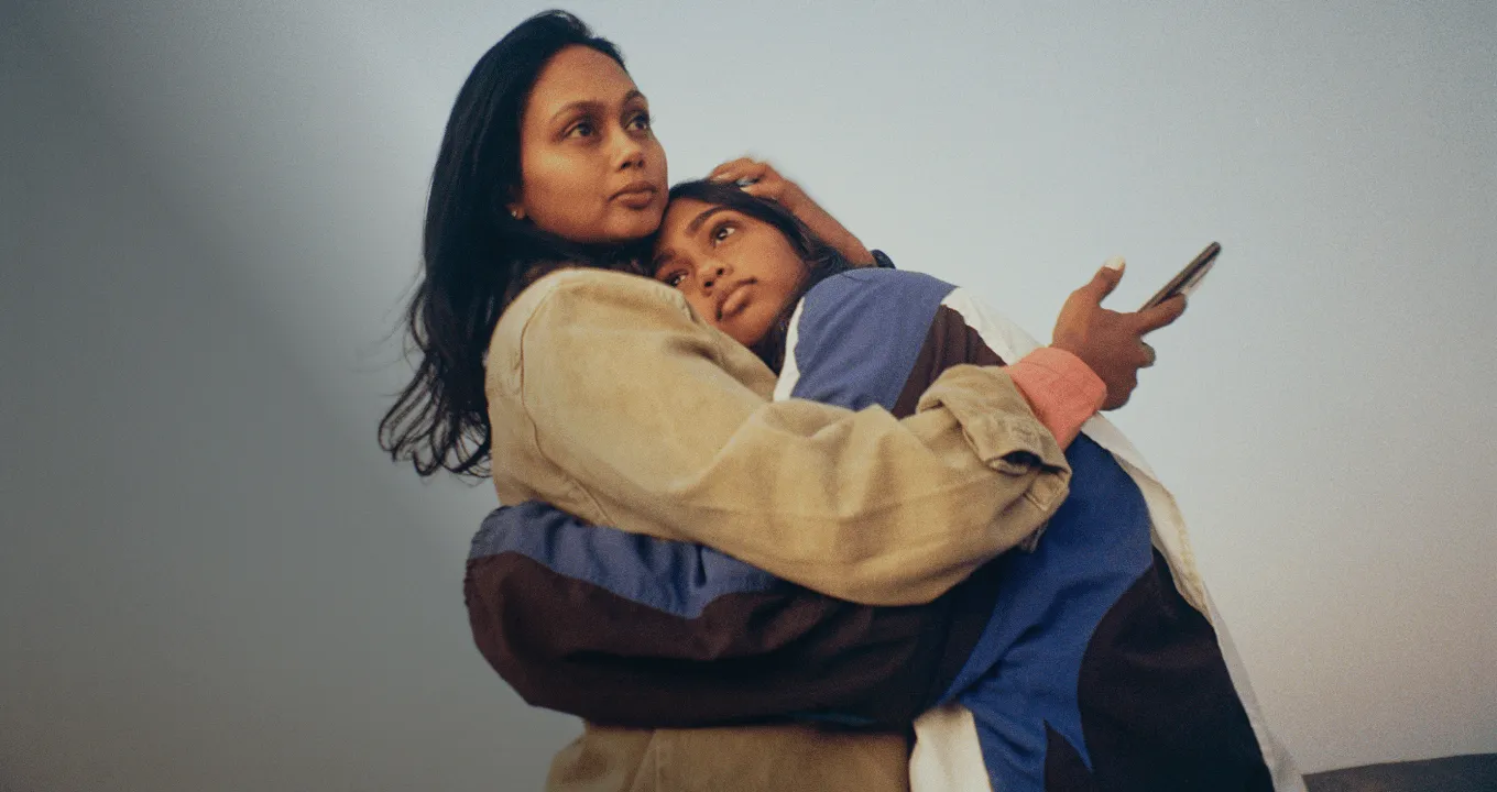 妈妈和女儿抱在一起，妈妈手里拿着手机